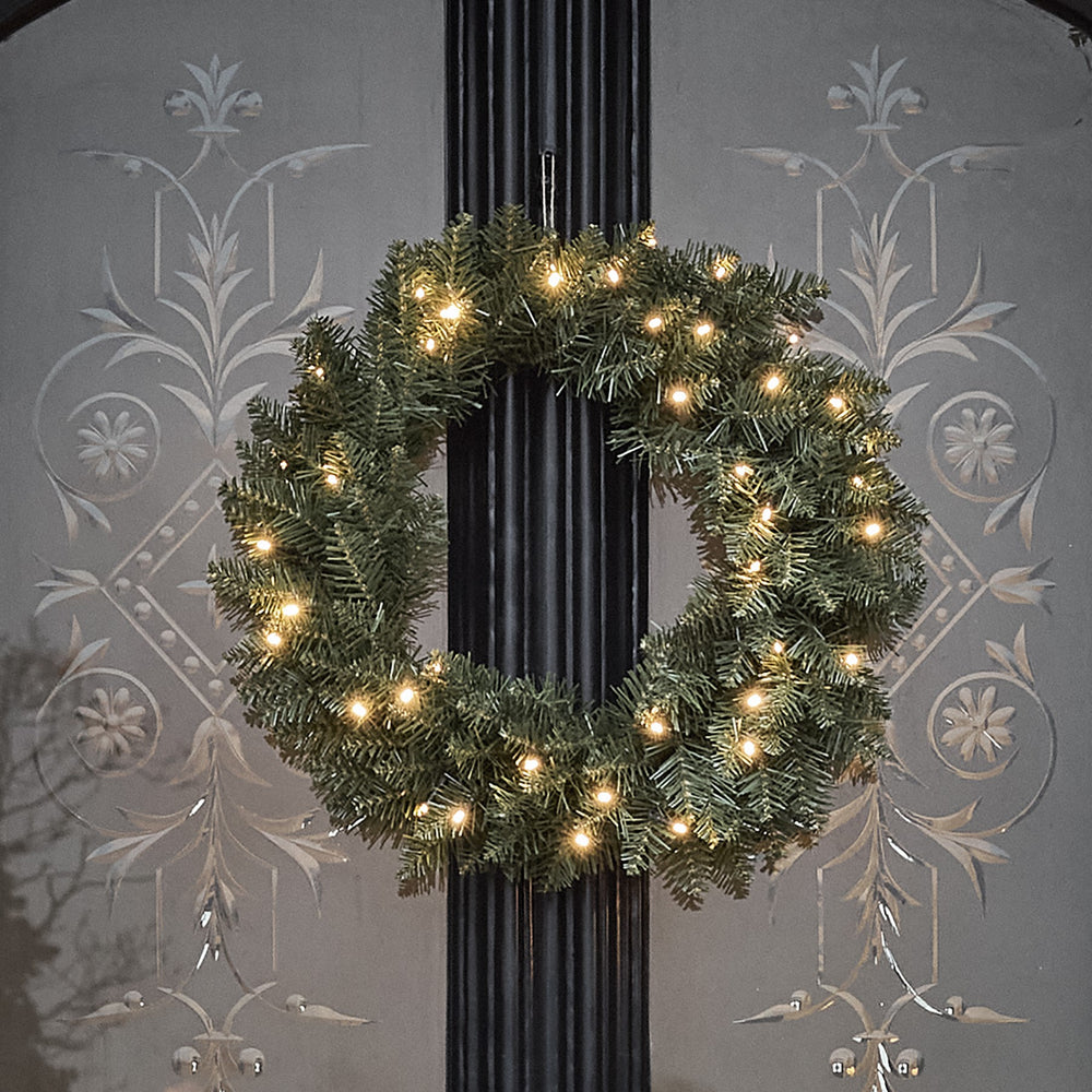 Beleuchteter Weihnachtskranz aus grünen Tannenzweigen mit warmweißen LEDs an schwarzer Tür