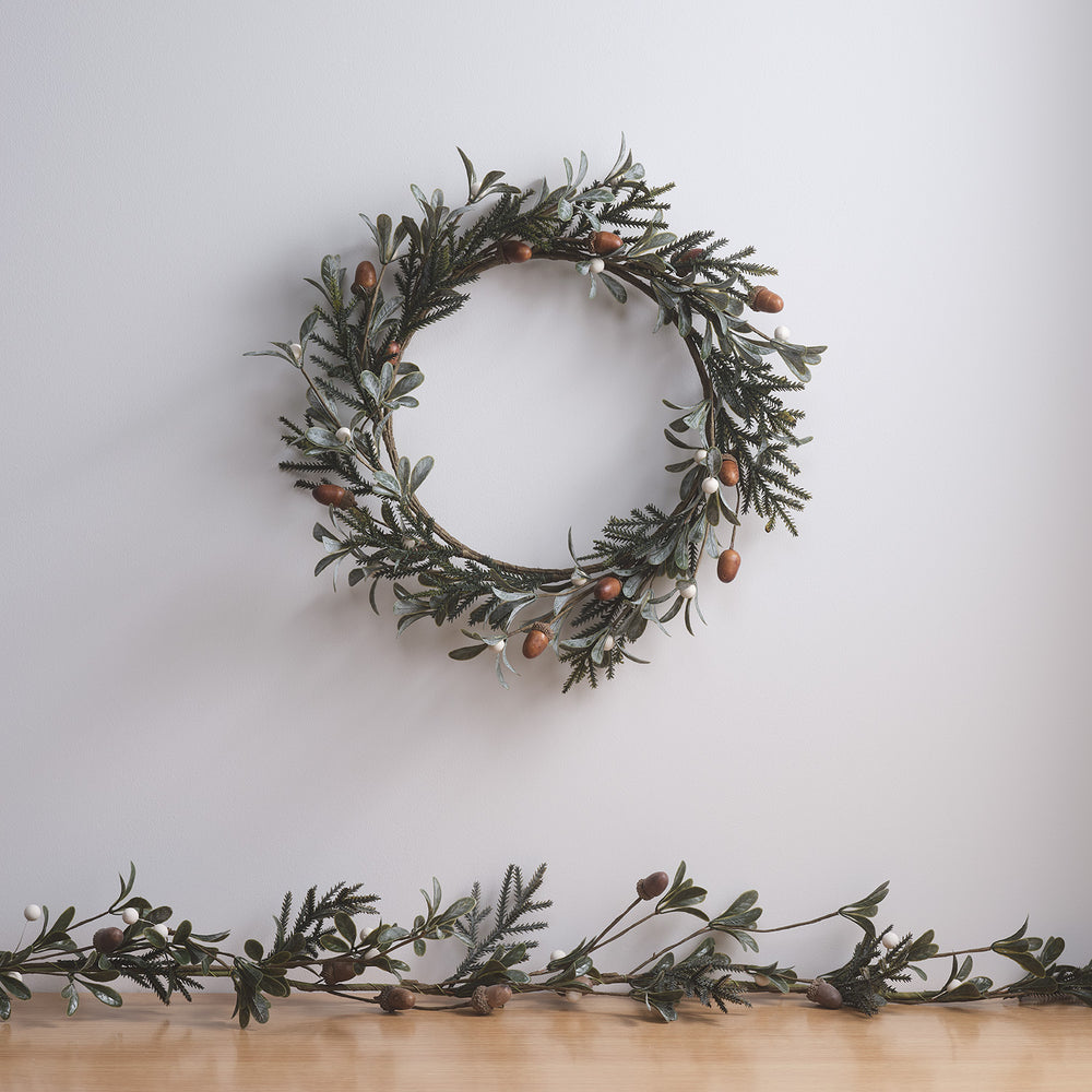 Weihnachtskranz mit Eicheln und weißen Beeren an Wand mit passender Girlande auf Holztisch