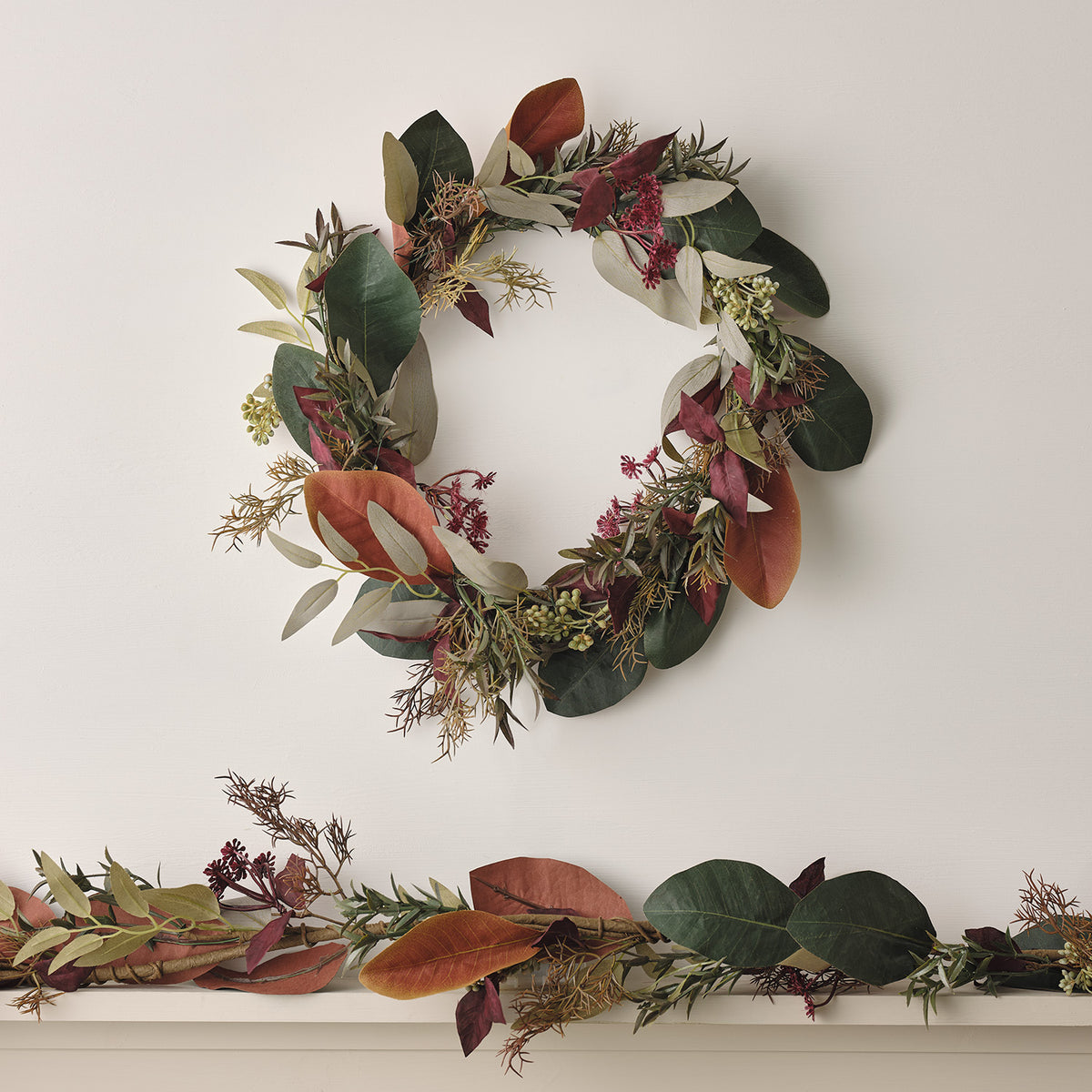 Herbstlicher Kranz mit grünen, roten und braunen Blättern an weißer Wand
