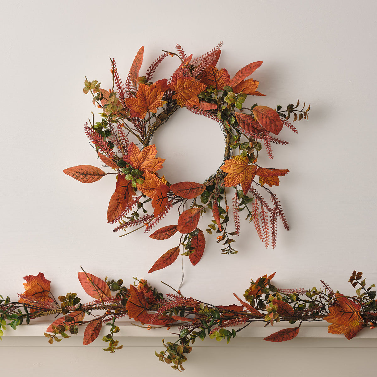 Herbstkranz mit orangefarbenen Ahornblättern und Girlande mit ähnlichen Blättern auf weißem Untergrund