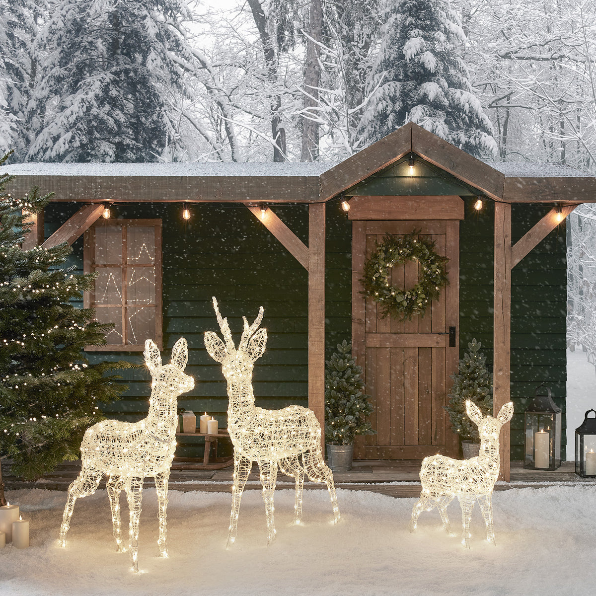 Weihnachtliche Rentierfamilie mit warmweißen LEDs vor verschneitem Holzhaus mit Türkranz