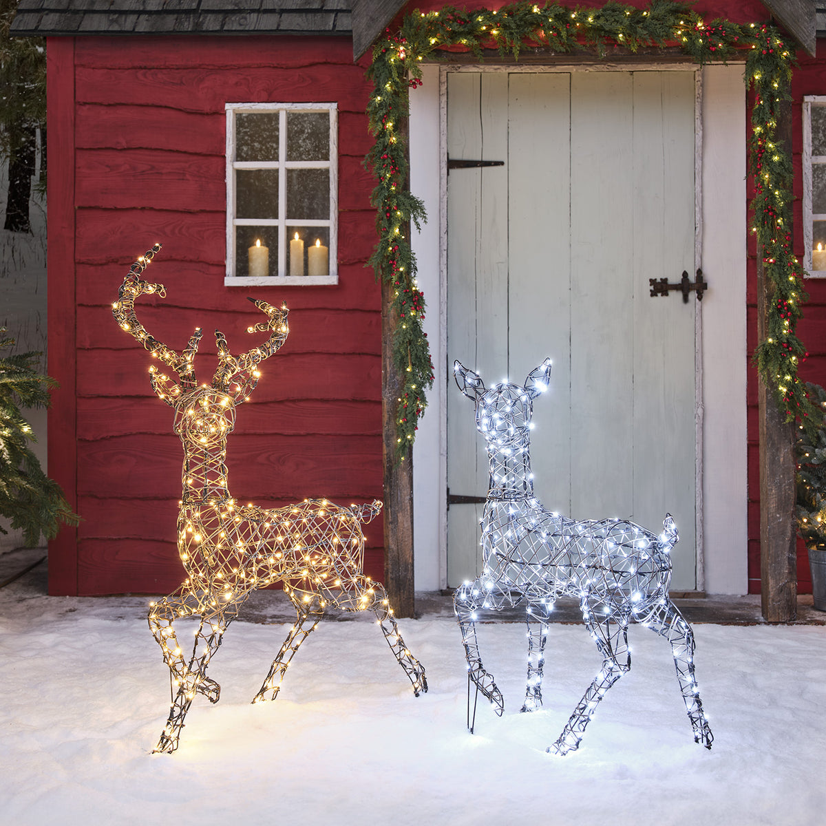 LED-Rentier Hirsch mit warmweißen und Hirschkuh mit kaltweißen Lichtern vor Haus im Schnee