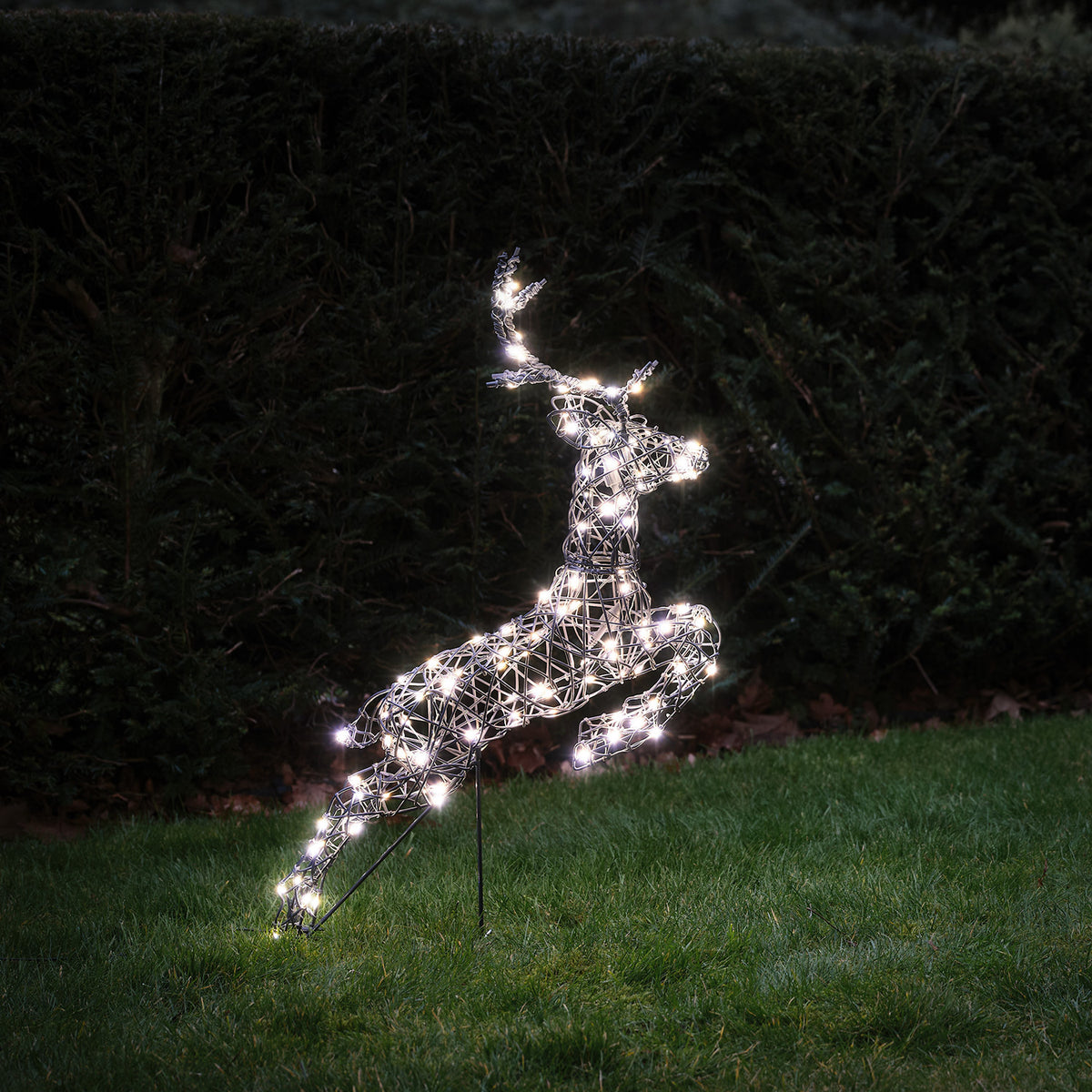 Einzelnes springendes LED-Rentier mit kaltweißen Lichtern auf grünem Rasen bei Nacht