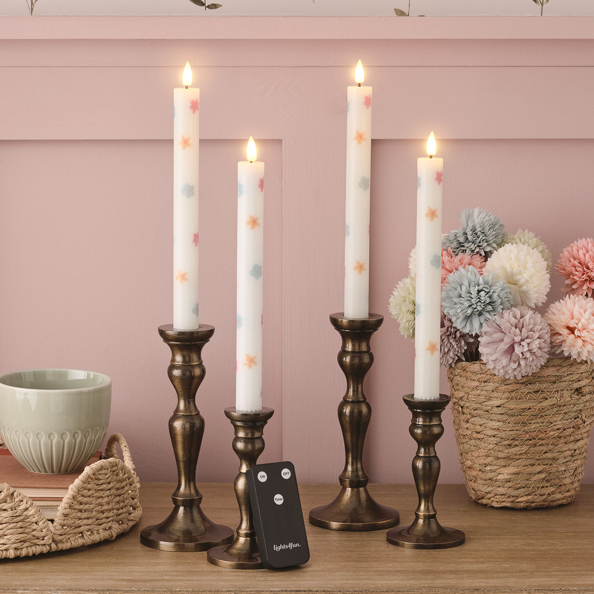 Vier LED Stabkerzen mit Blumenmuster in Kerzenhaltern und Fernbedienung auf Holztisch