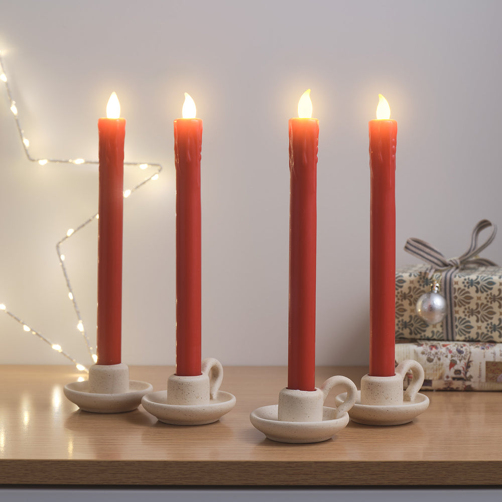 Vier brennende rote LED Tafelkerzen in weißen Kerzenhaltern vor Weihnachtsgeschenken und Lichterkette