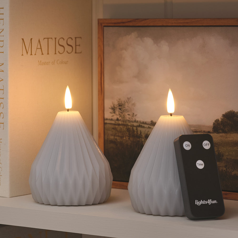 Zwei hellgraue LED-Echtwachskerzen im Pear-Design mit Fernbedienung auf Regal vor Bildern