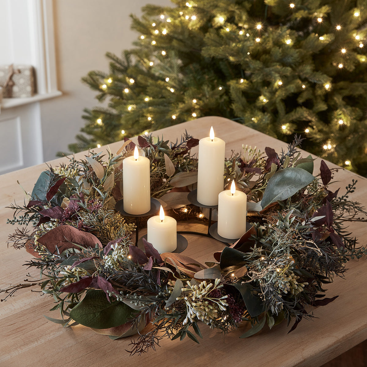 Herbst- und Winterkranz mit roten Beeren, Eukalyptus, Laub und vier elfenbeinfarbenen LED-Kerzen auf einem Holztisch