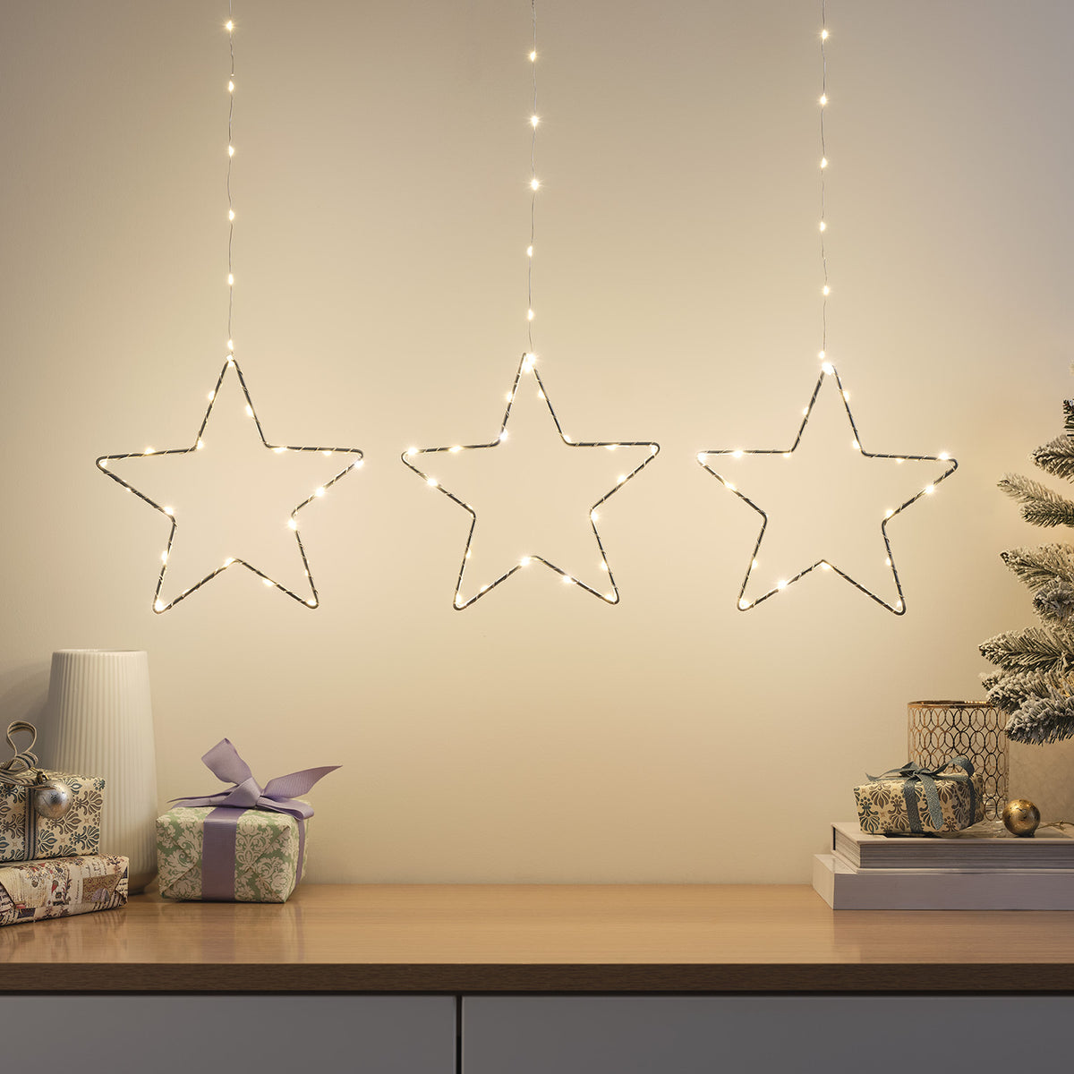 Drei leuchtende LED-Sterne hängen an einer Wand über einem Tisch mit Geschenken