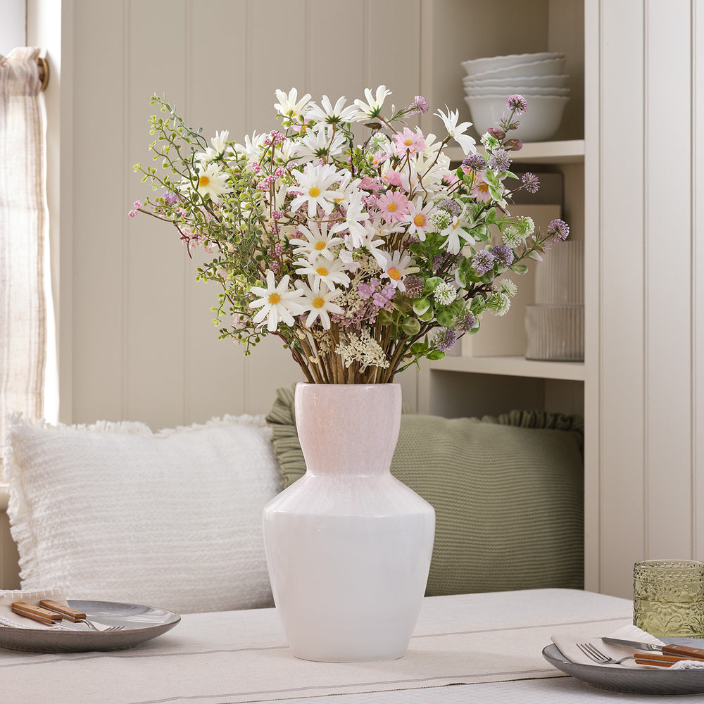 Kunstblumenstrauß mit weißen und rosa Gänseblümchen in rosa-weißer Keramikvase auf Tisch