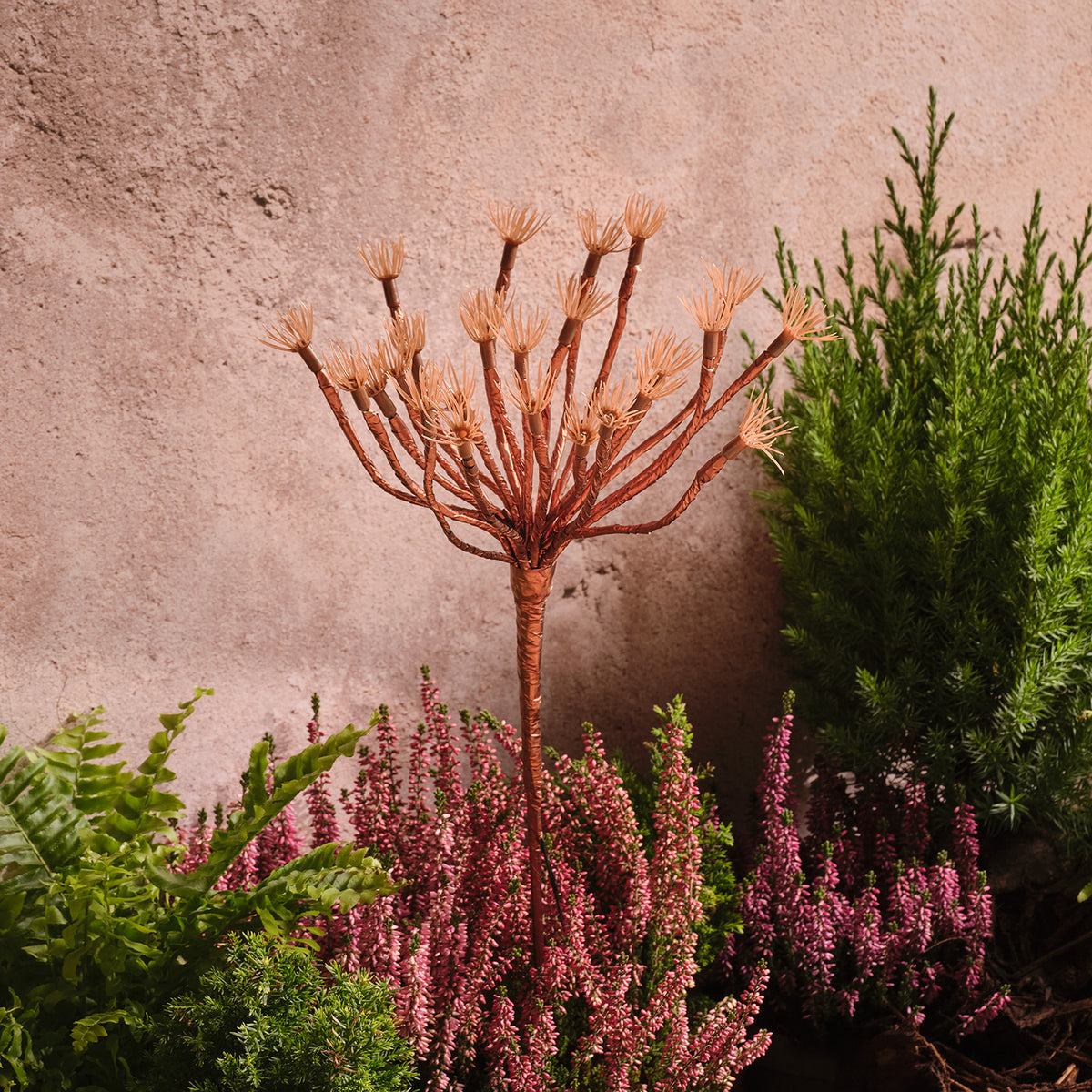 Drei goldfarbene Pusteblumen-Gartenstecker ohne Beleuchtung im Beet vor einer Wand
