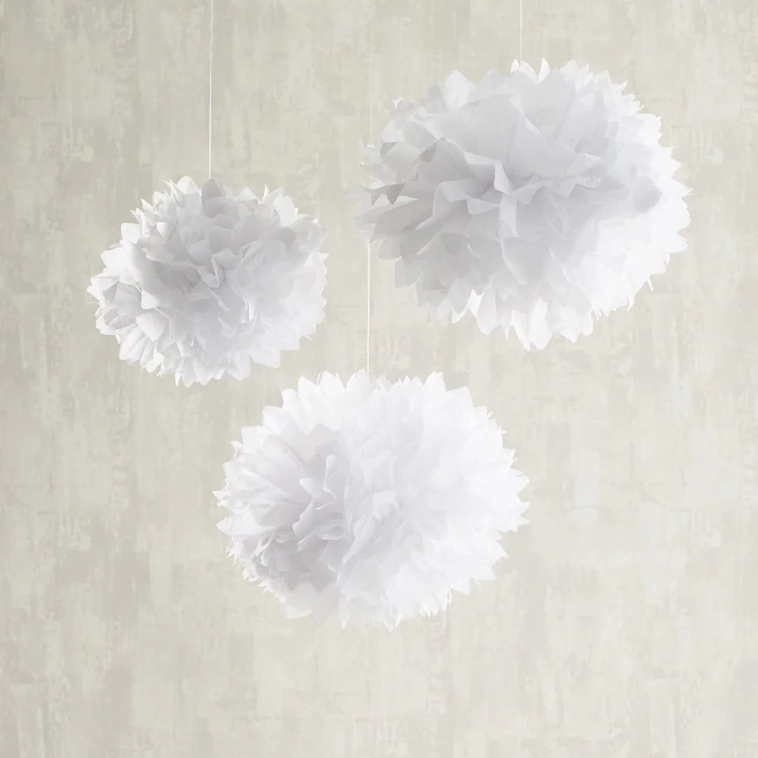 Drei weiße Papierpompons in verschiedenen Größen hängen an weißen Schnüren vor hellem Hintergrund