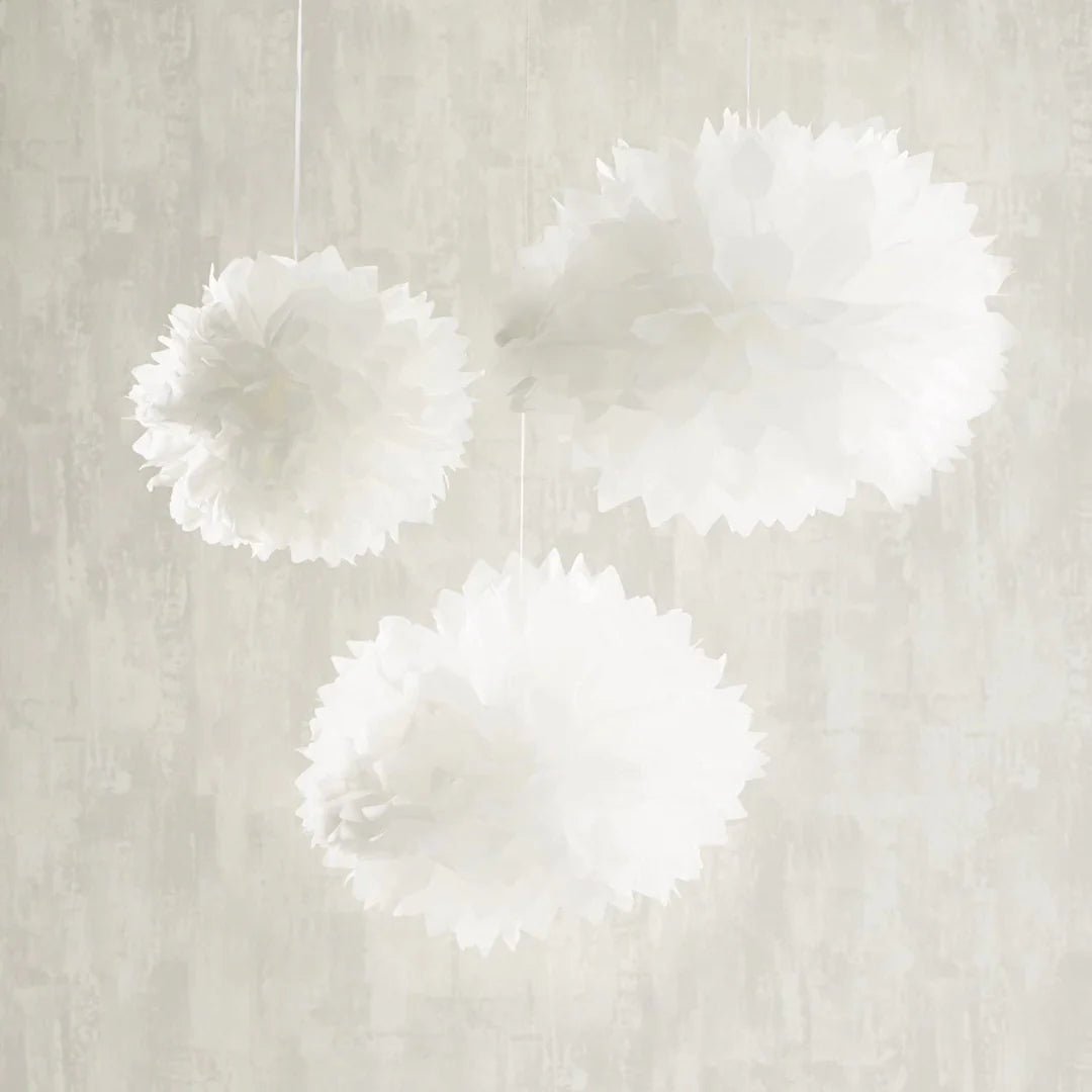 Drei weiße Papierpompons in unterschiedlichen Größen von unten fotografiert, hängend an weißen Schnüren
