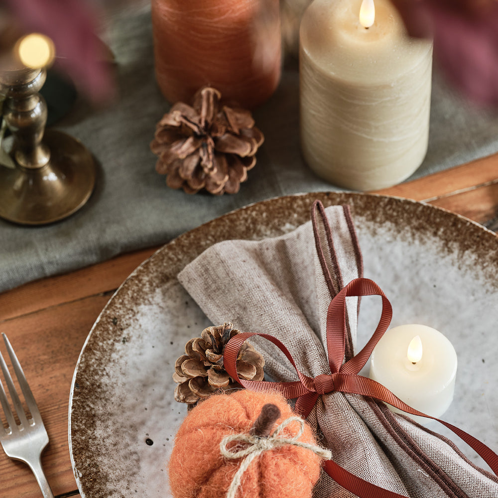 Herbstliche Tischdeko mit Filz-Kürbis, Zapfen, Kerzen und Stoffserviette auf Teller