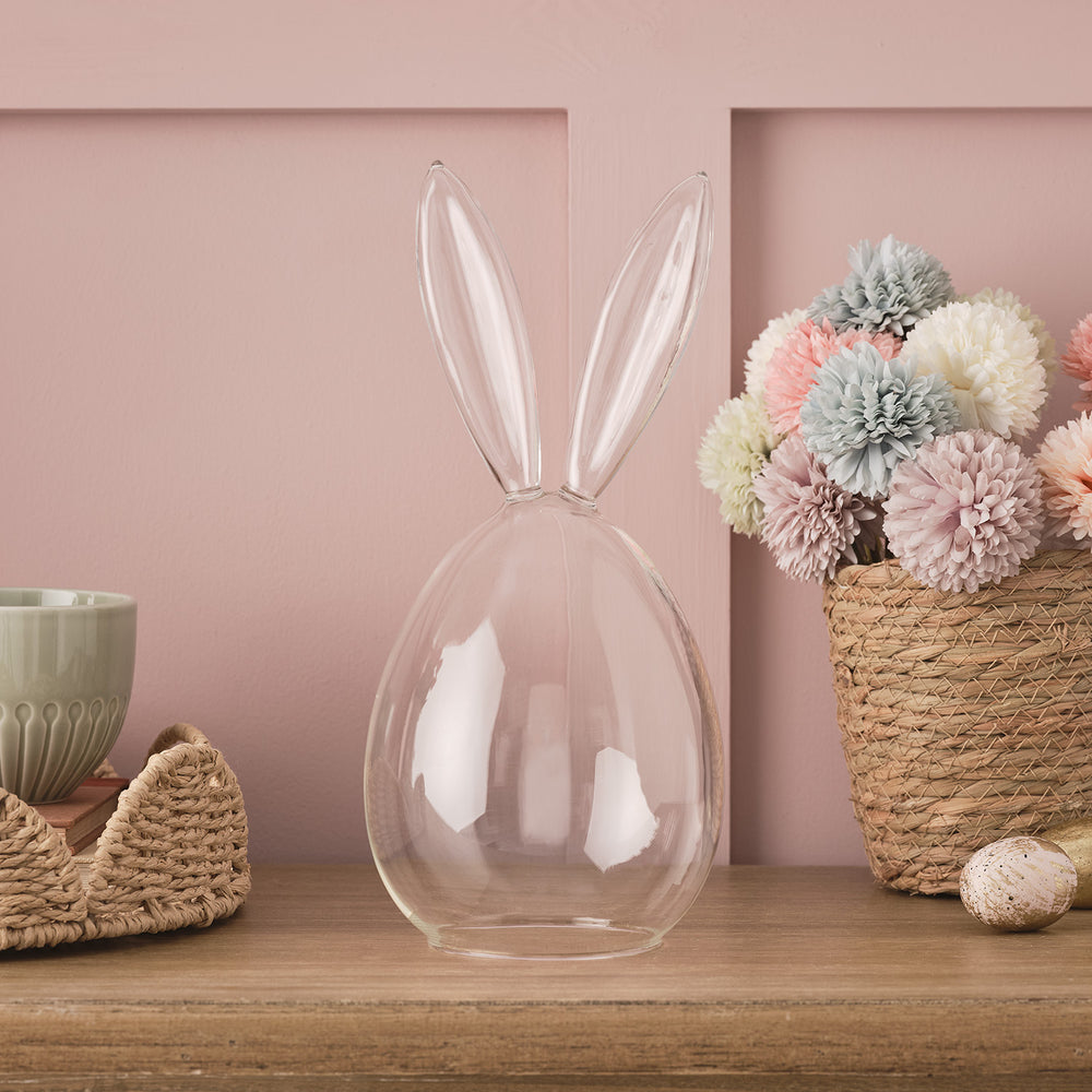 Glaskuppel mit Hasenohren vor rosa Wand neben Korb mit pastellfarbenen Blumen