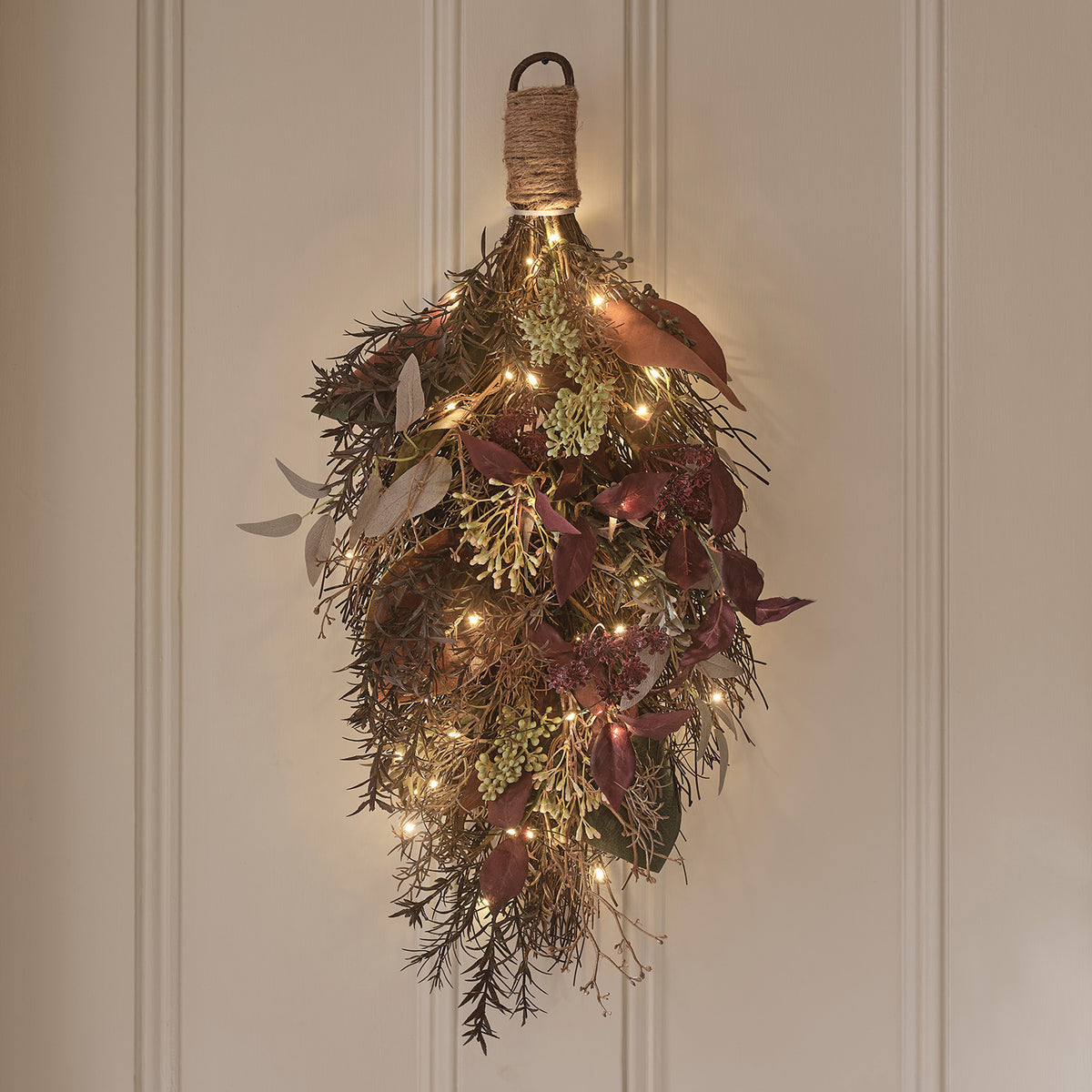Herbstlicher Wandzweig mit Juteband und warmweißen LED-Lichtern an einer hellen Wand