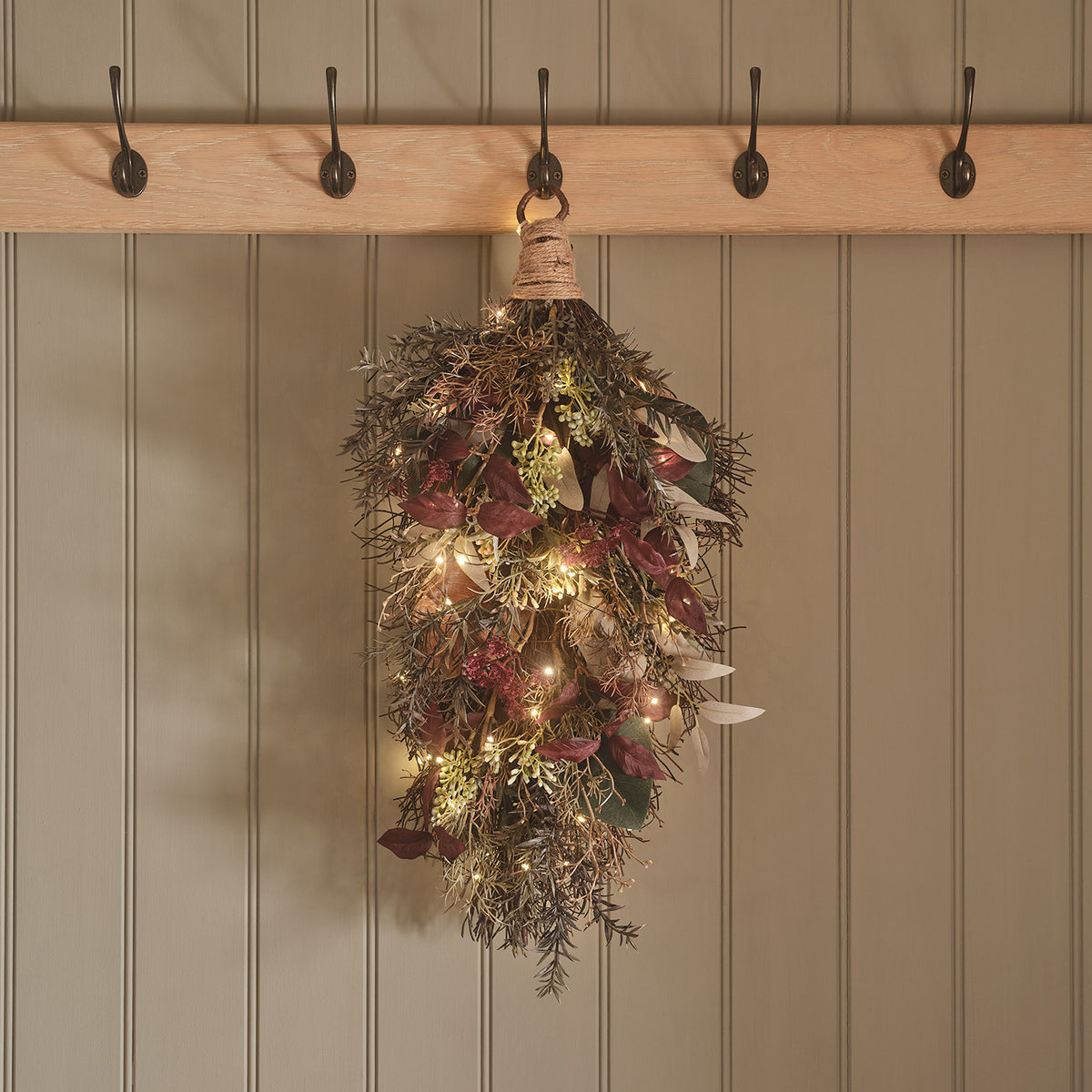 Herbstzweig mit LED-Lichterkette hängt an einem Haken an einer Garderobe mit fünf Haken