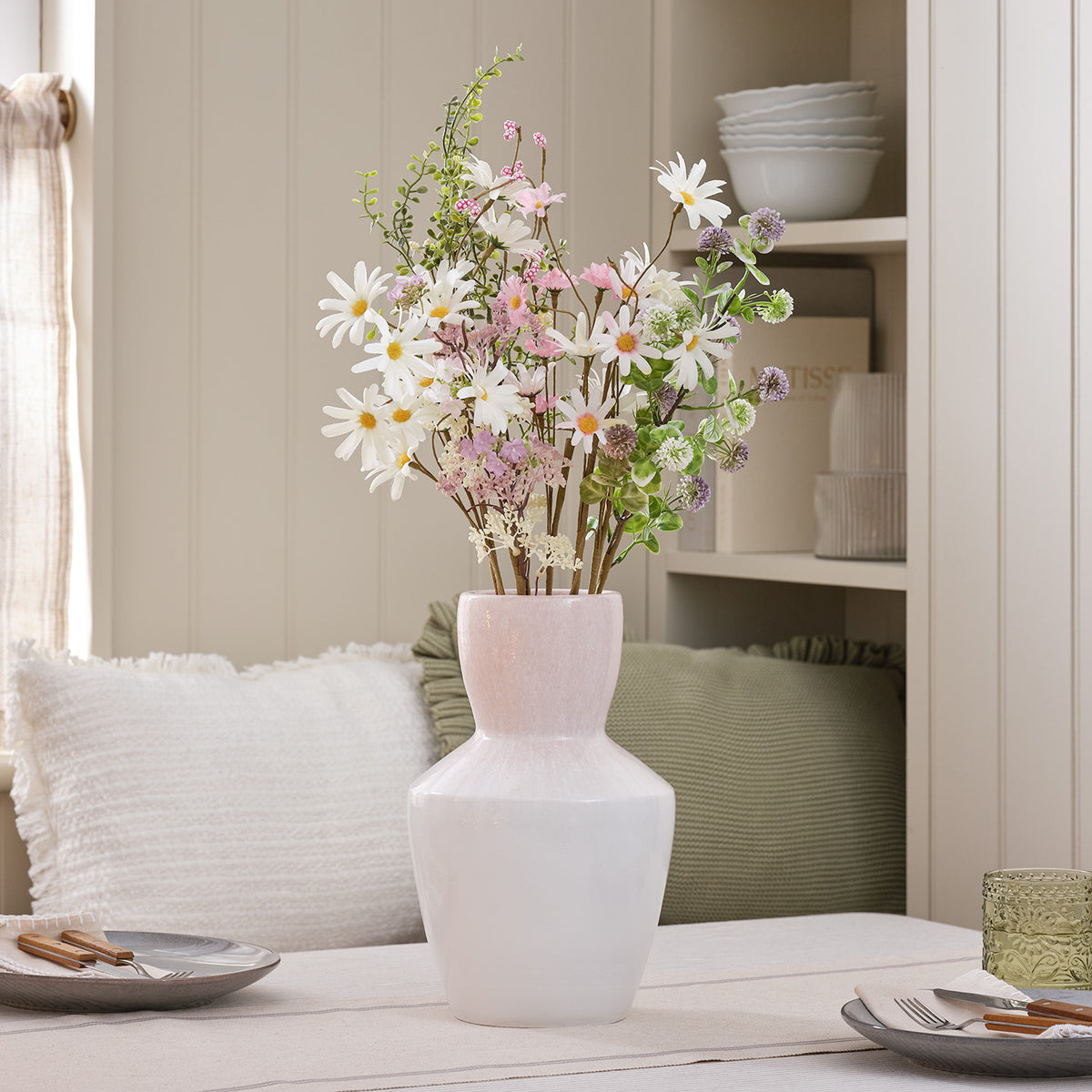 Künstlicher Frühlingsstrauß mit weißen und rosa Gänseblümchen in großer rosa-weißer Vase auf Tisch