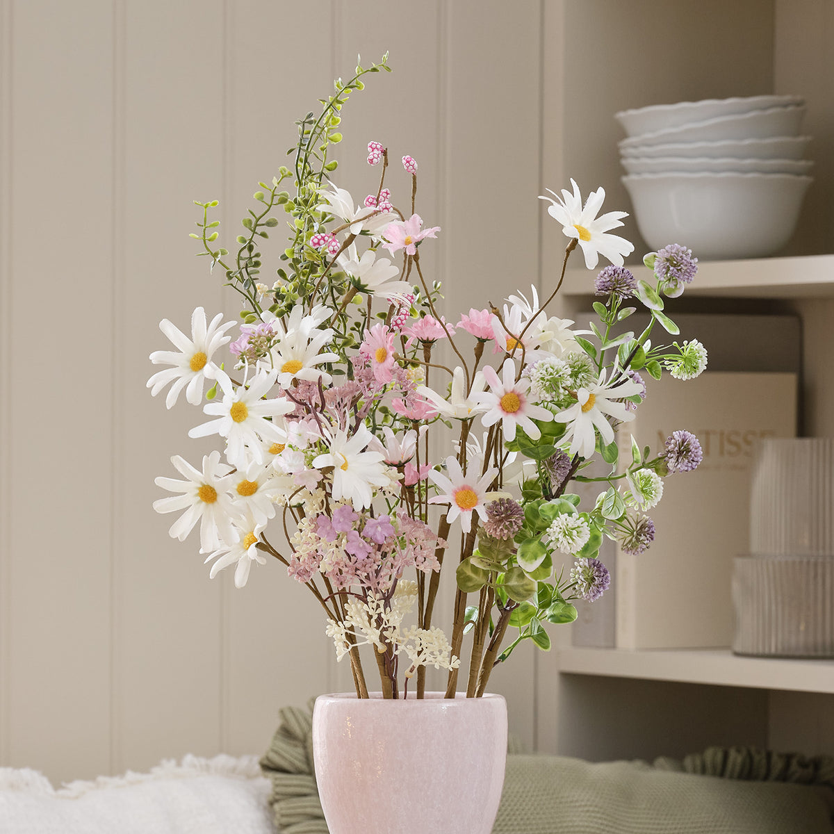 Künstlicher Frühlingsstrauß mit weißen und pastellrosa Gänseblümchen in rosa Vase vor Regal