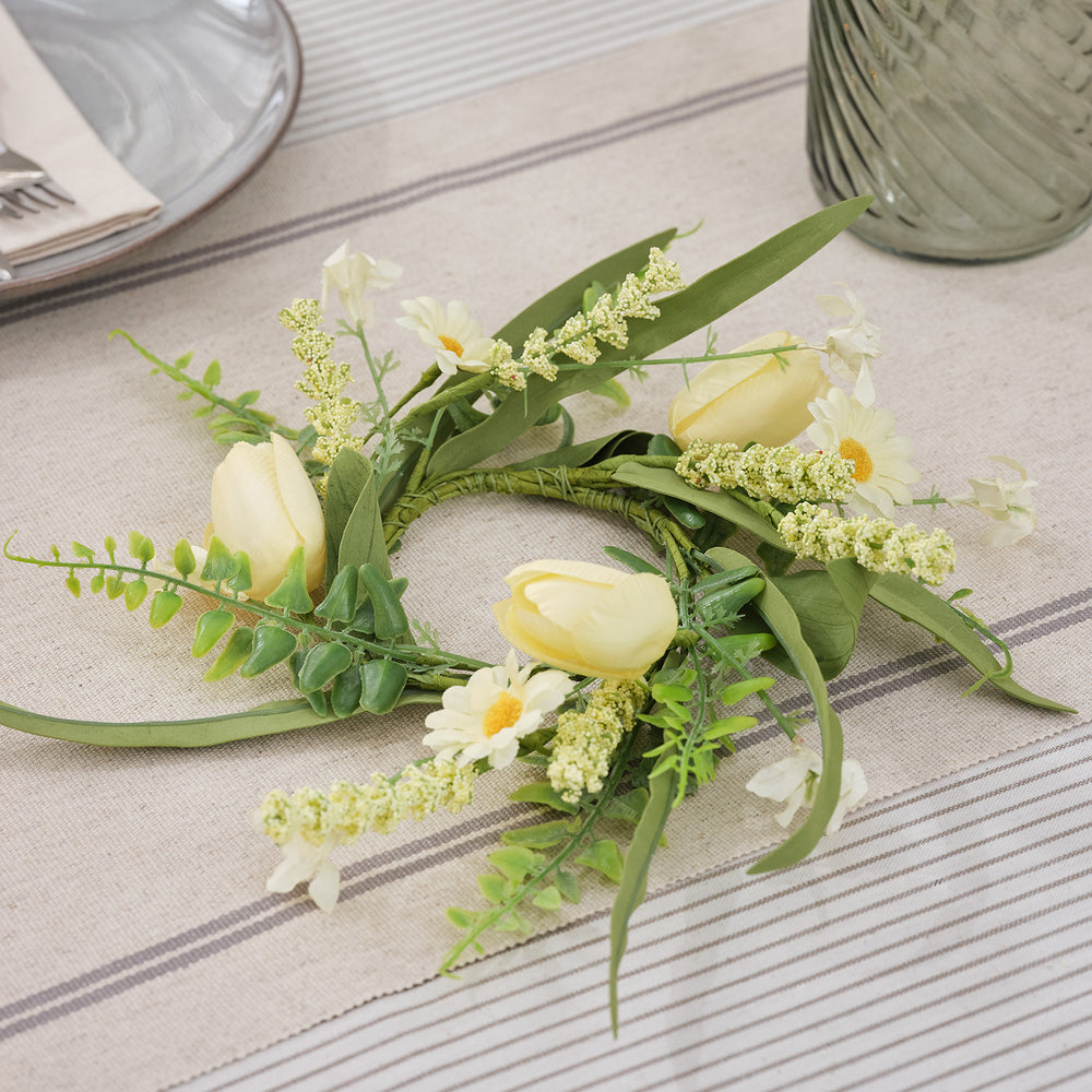 Kerzenring mit buttergelben Tulpen, Gänseblümchen und grünen Gräsern auf Tischdecke