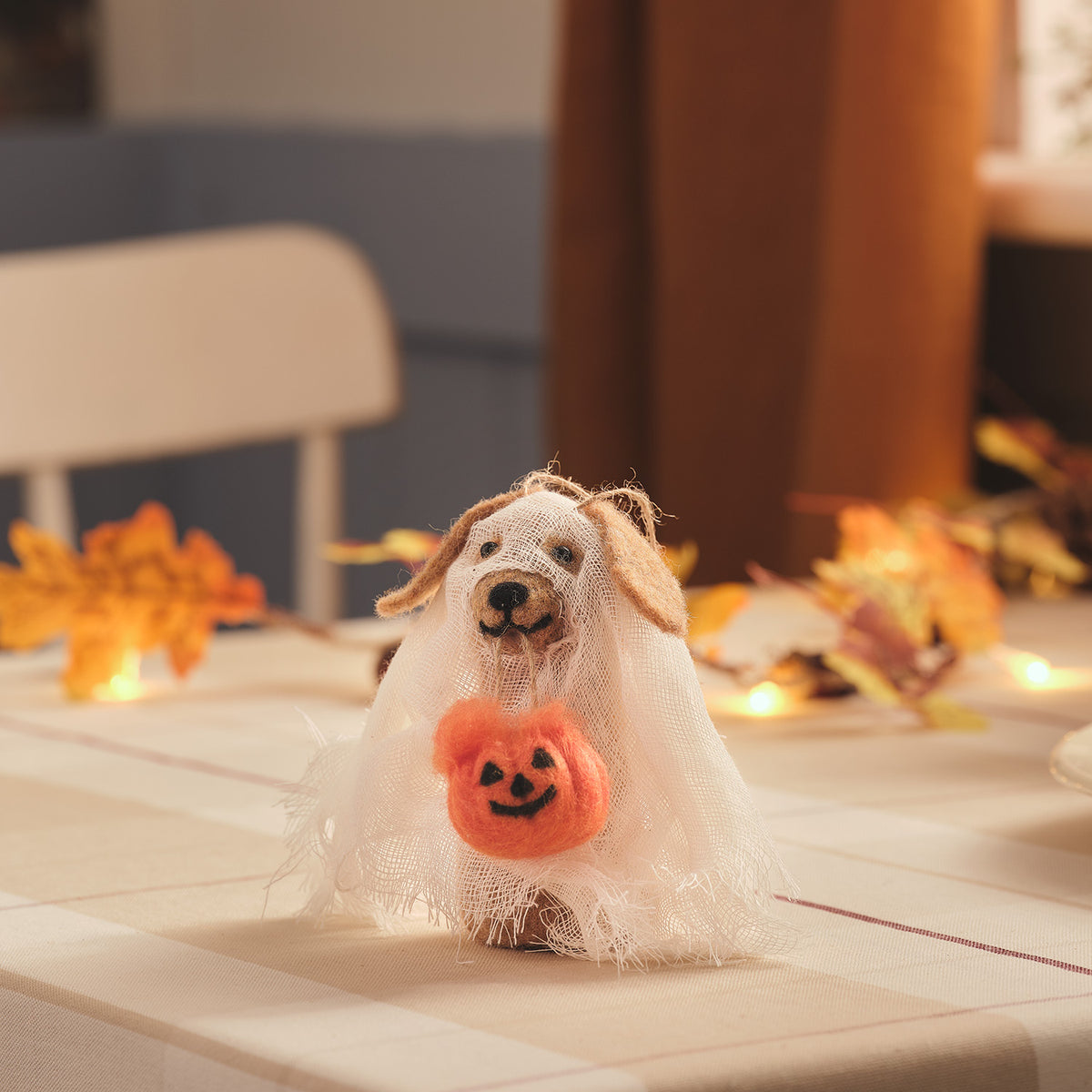 Halloween-Hund aus Filz mit Geisterumhang und orangefarbenem Kürbis als Dekoration auf Tisch