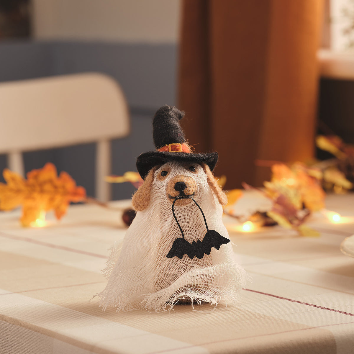 Halloween-Hund aus Filz mit Geisterumhang, schwarzem Hexenhut und Fledermaus im Maul auf Tisch