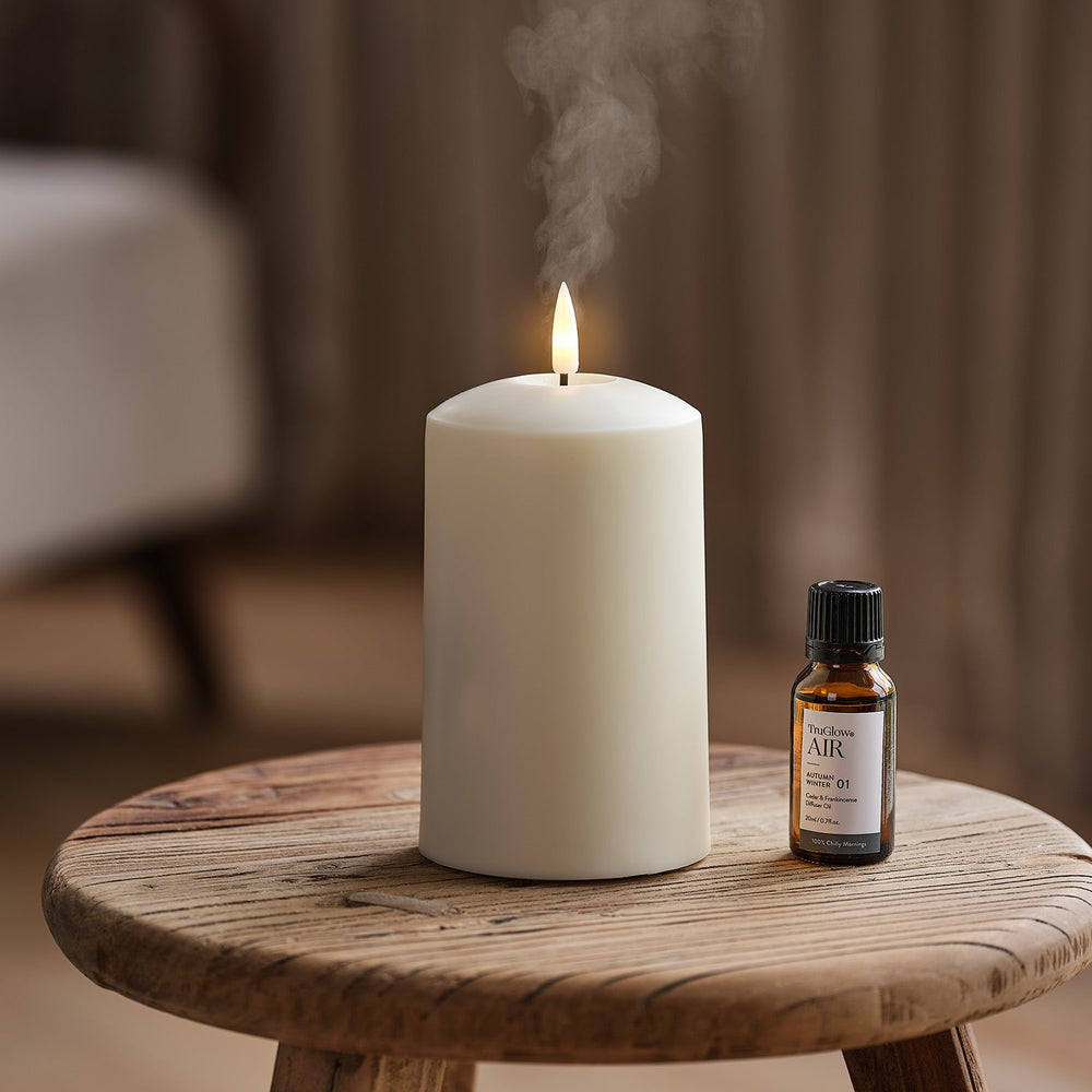 Weißer Kerzendiffusor mit Flamme und Dampf neben TruGlow AIR Duftölflasche auf Holzstuhl