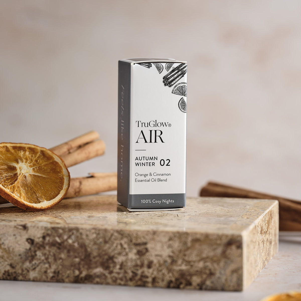 Verpackung TruGlow AIR ätherisches Öl Orange & Zimt neben getrockneter Orangenscheibe und Zimtstangen