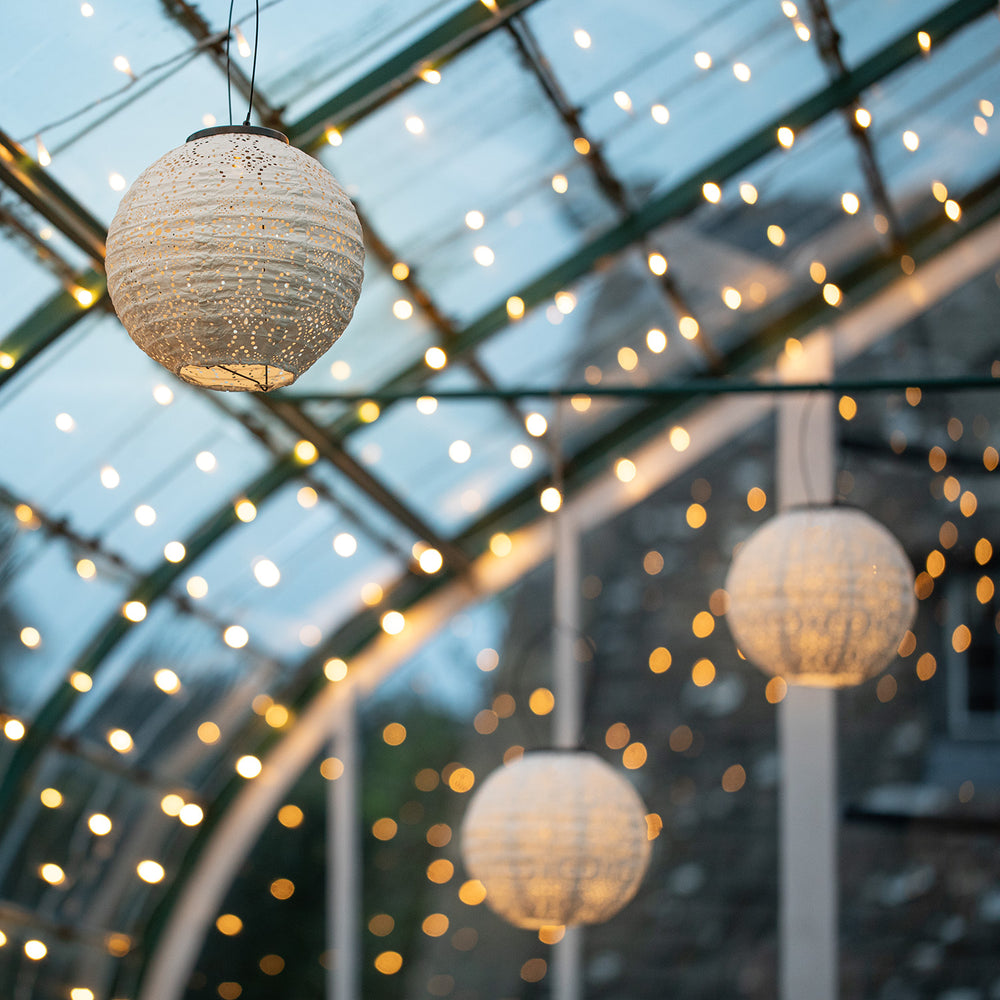Nahaufnahme von weißen, leuchtenden Tyvek-Solarlampion-Lampen vor einem mit Lichterketten geschmückten Glasdach