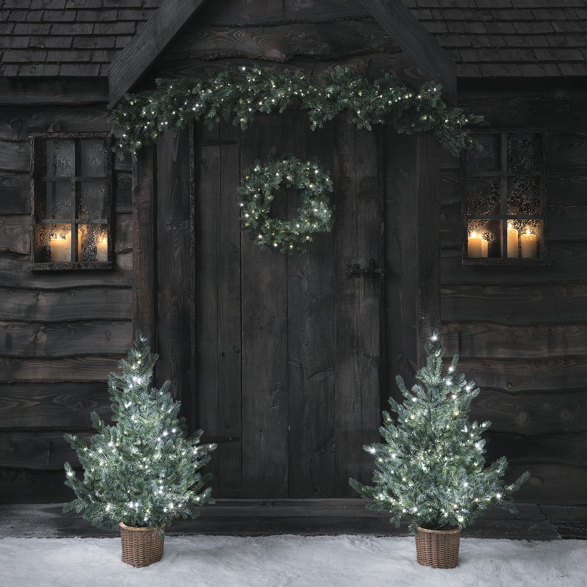 Weihnachtskranz und Girlande mit kaltweißem LED-Licht an dunkler Holztür ohne Weihnachtsbäume
