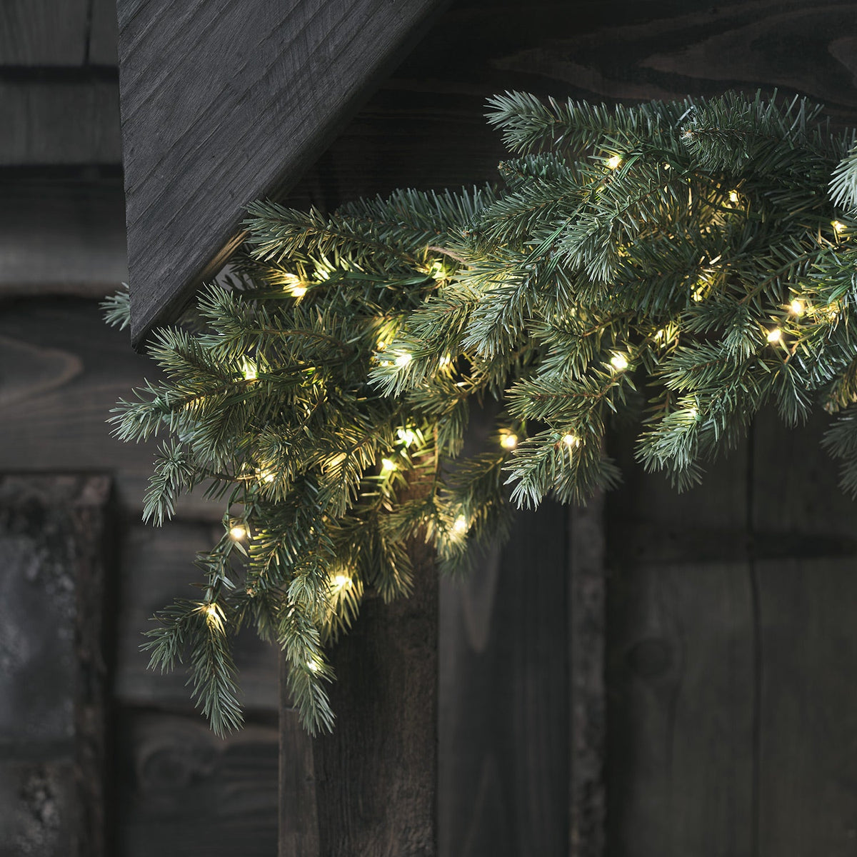 Nahaufnahme einer beleuchteten Weihnachtsgirlande mit warmweißen LEDs an Holzwand