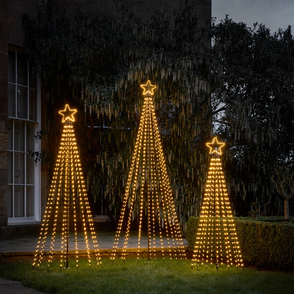 Drei LED-Weihnachtsbäume in verschiedenen Größen mit warmweißen Lichtern und Sternen auf einer Terrasse