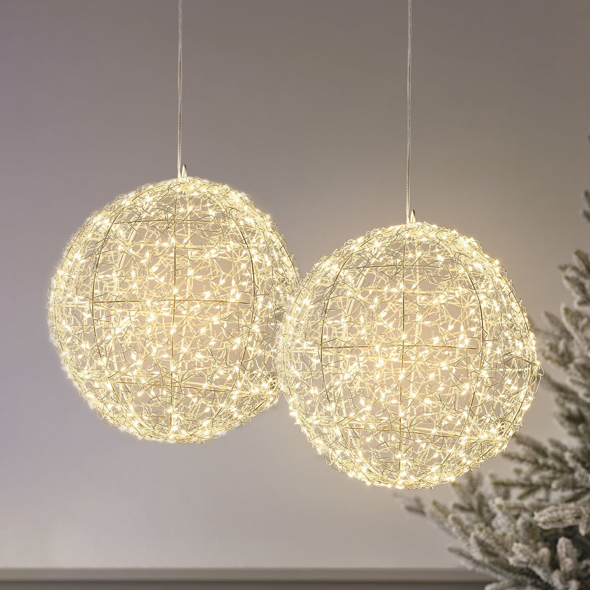 Zwei große Drahtkugeln mit warmweißen Micro-LEDs hängen vor grauem Hintergrund