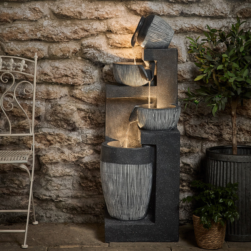 Darnbrook LED Gartenbrunnen mit dreistufigem Wasserkaskade vor Steinwand und Pflanzen