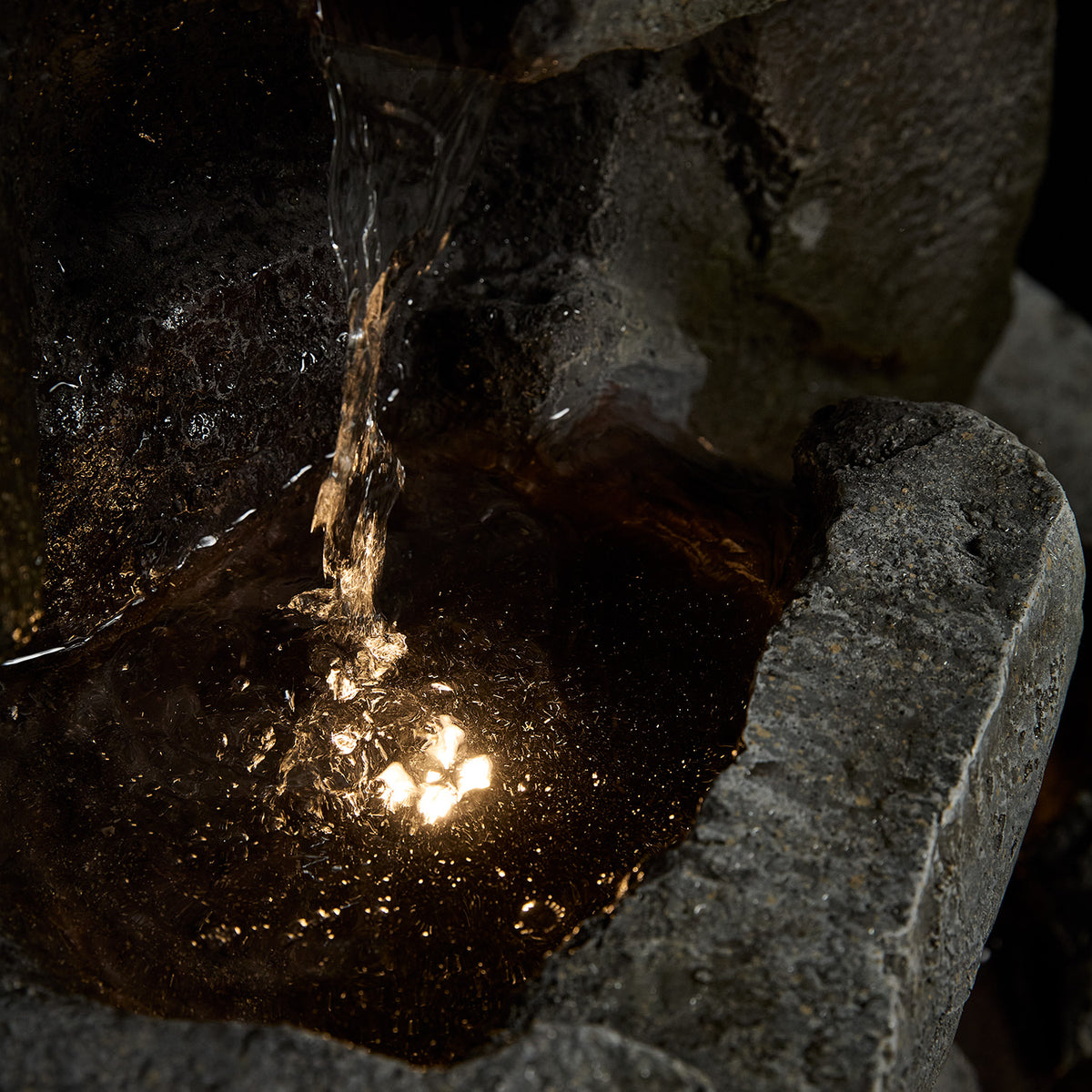 Detailaufnahme des Wasserlaufs und der warmweißen LED-Beleuchtung im Gartenbrunnen aus Steinoptik