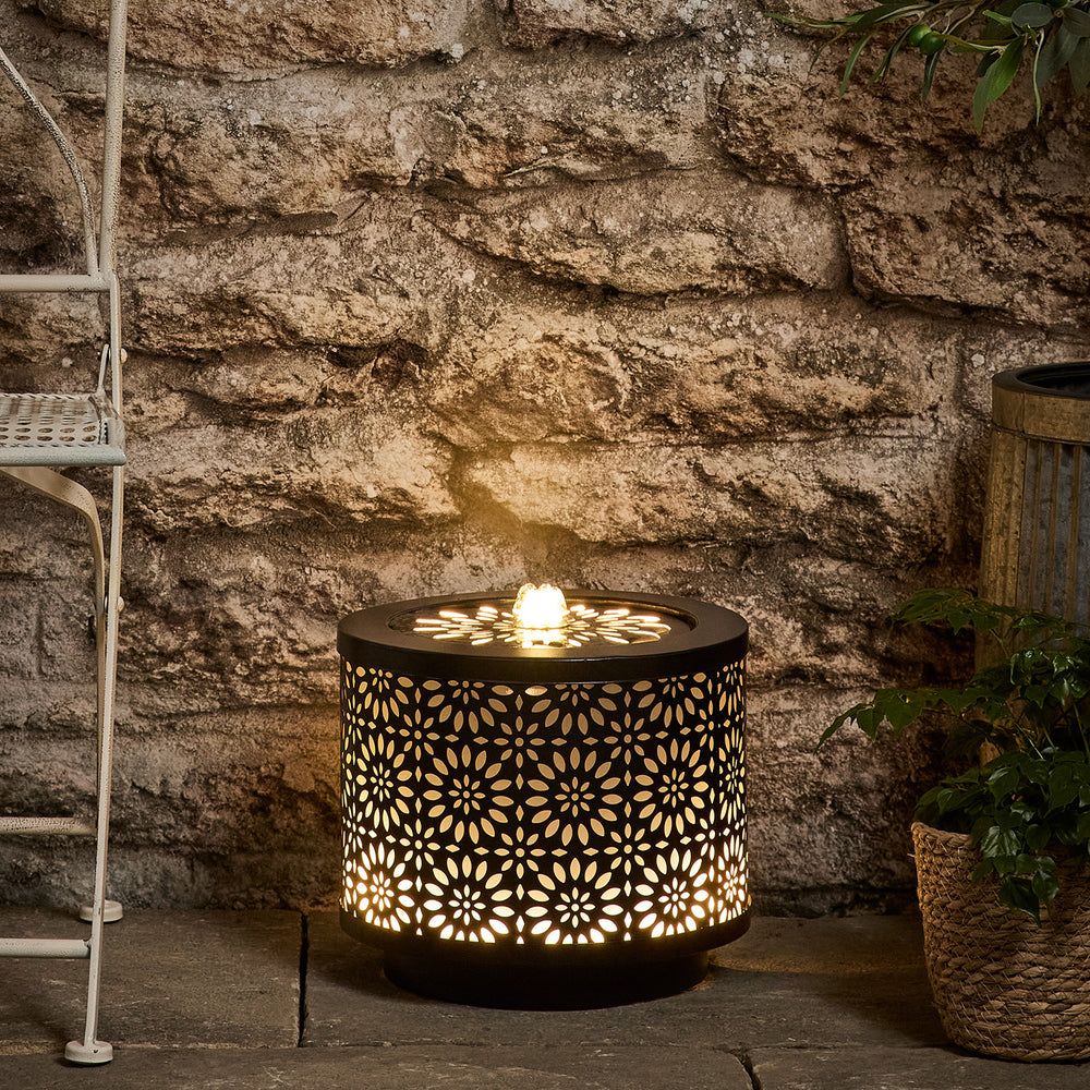 Beleuchteter Lucia LED Gartenbrunnen mit floralem Muster vor Steinwand und Pflanzen