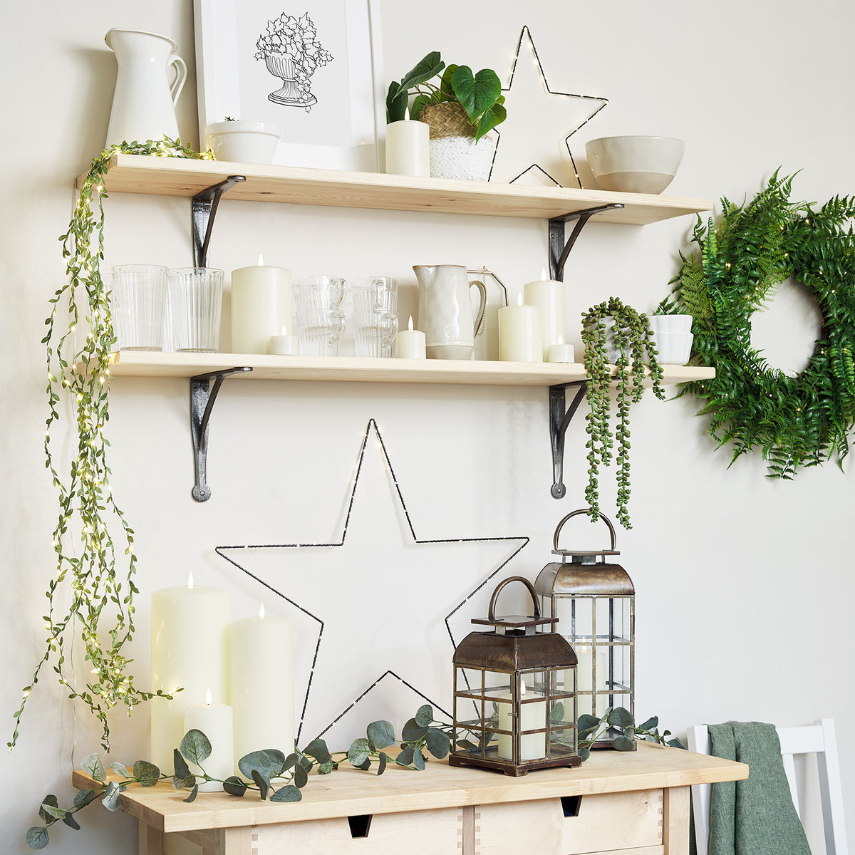 Zwei messingfarbene Laternen mit Glasfenstern auf Holzkommode unter Holzregalen mit Dekoration