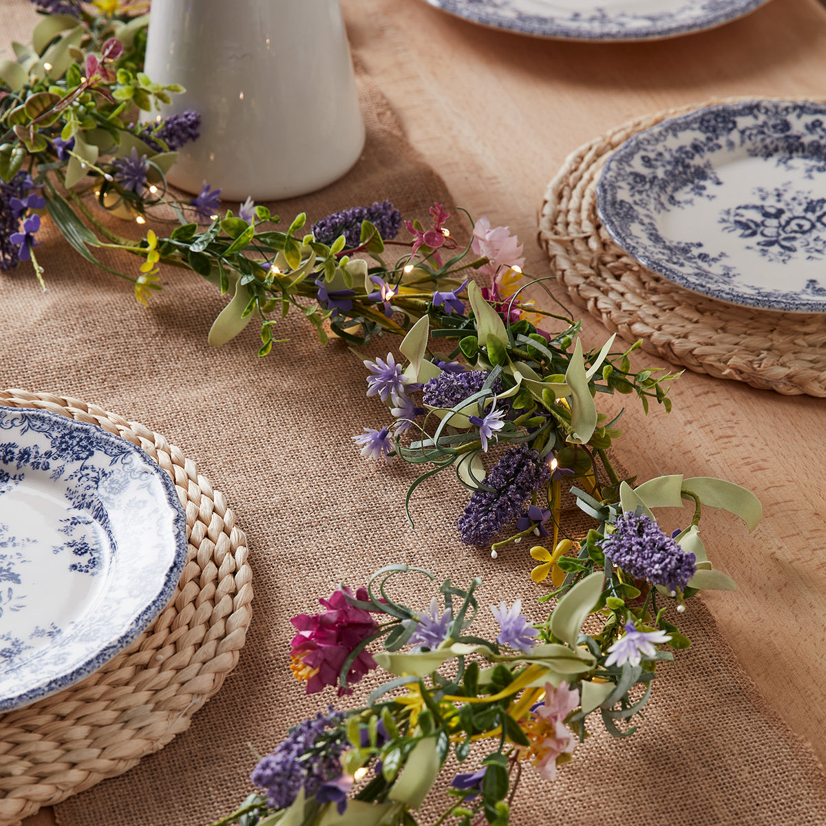 Frühlingsgirlande mit Lavendel und bunten Blumen auf gedecktem Holztisch mit blau-weißem Geschirr