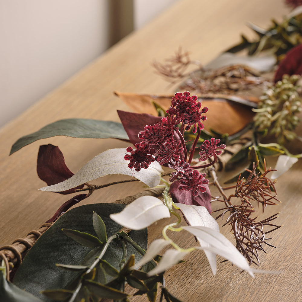 Nahaufnahme der herbstlichen Girlande mit roten Blüten und verschiedenen Blättern auf hellem Holztisch