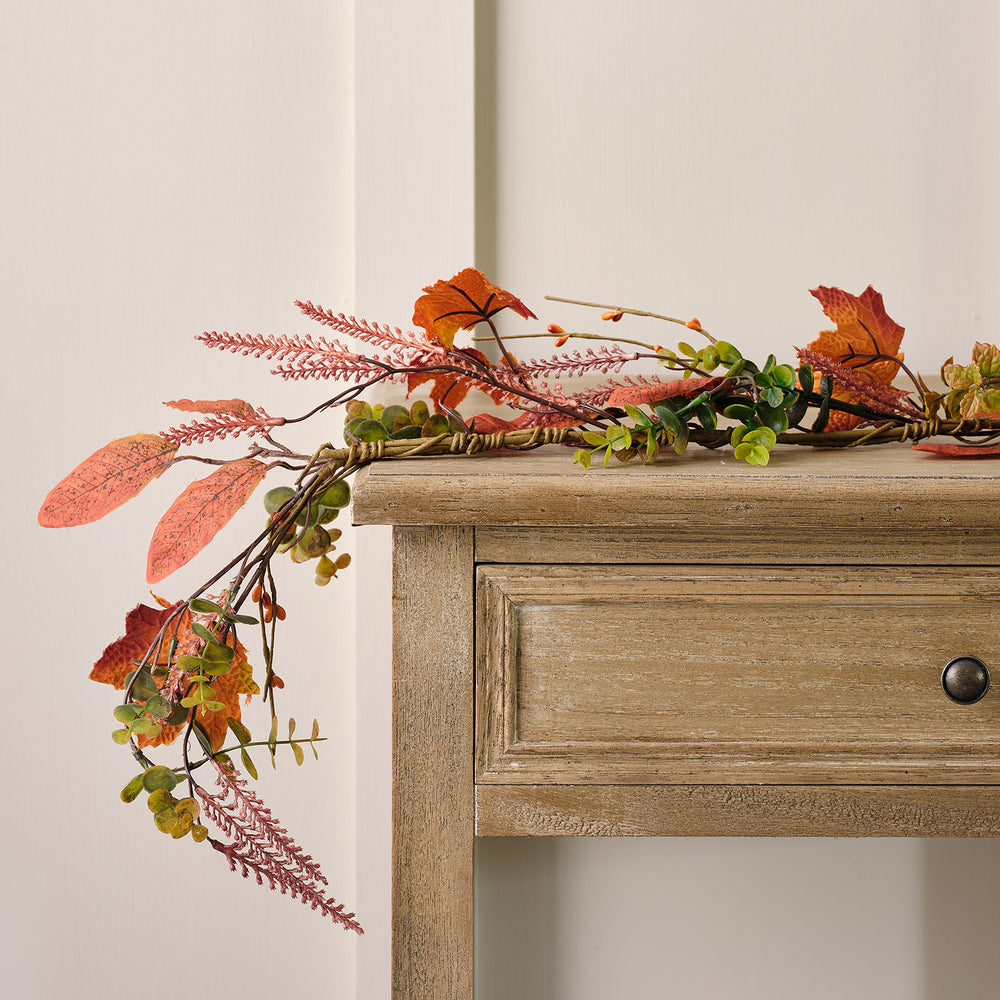 Herbstgirlande mit orangefarbenen Ahornblättern und grünen Zweigen auf einem Holztisch