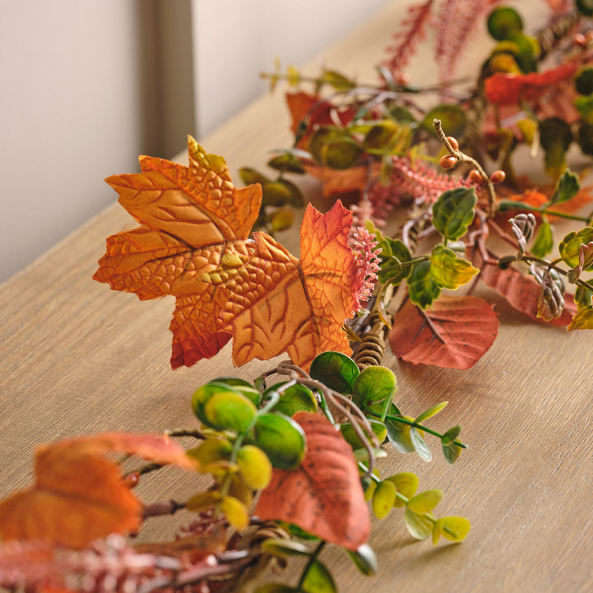 Nahaufnahme der Herbstgirlande mit detaillierten orangefarbenen Ahornblättern und grünen Blättern