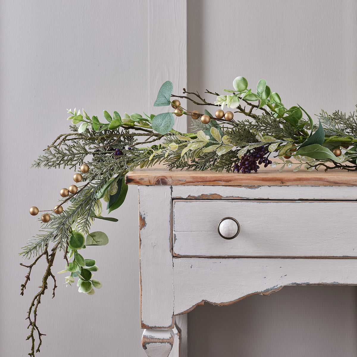 Weihnachtsgirlande mit goldenen Beeren und grünen Blättern auf weißem Holzkommode drapiert