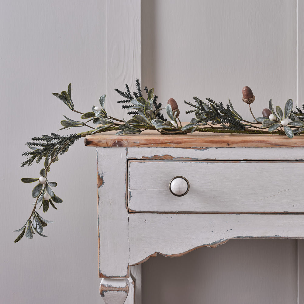 Weihnachtsgirlande mit künstlichen Eicheln, weißen Beeren und grünem Laub auf einem weißen Holztisch