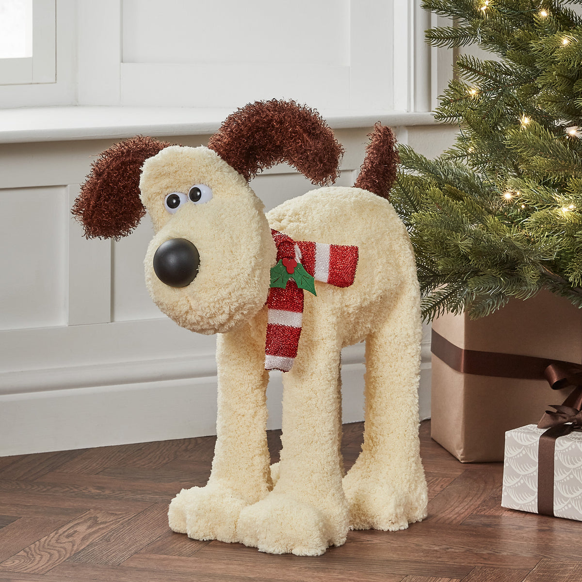 Gromit LED-Figur mit rot-weißem Schal vor Weihnachtsbaum und Geschenken auf Holzboden