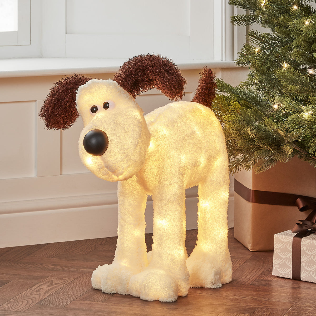 Beleuchtete Gromit LED-Figur mit rot-weißem Schal vor dunklem Hintergrund und Kerzen