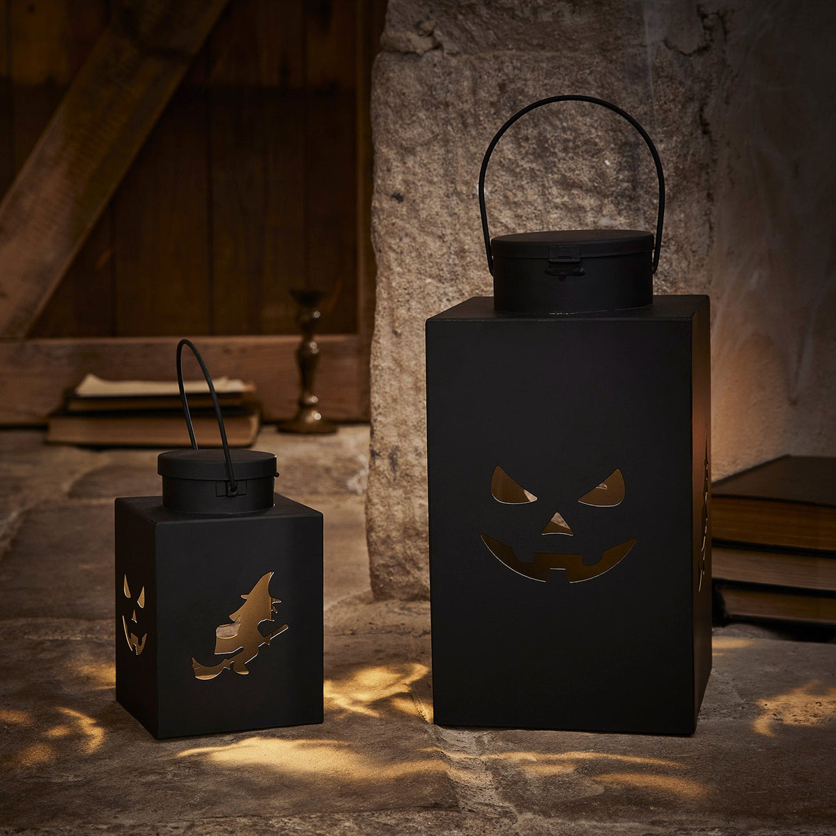 Schwarze Halloween-Laternen mit ausgeschnittenen Hexen und Kürbisgesichtern, warm beleuchtet vor Steinwand