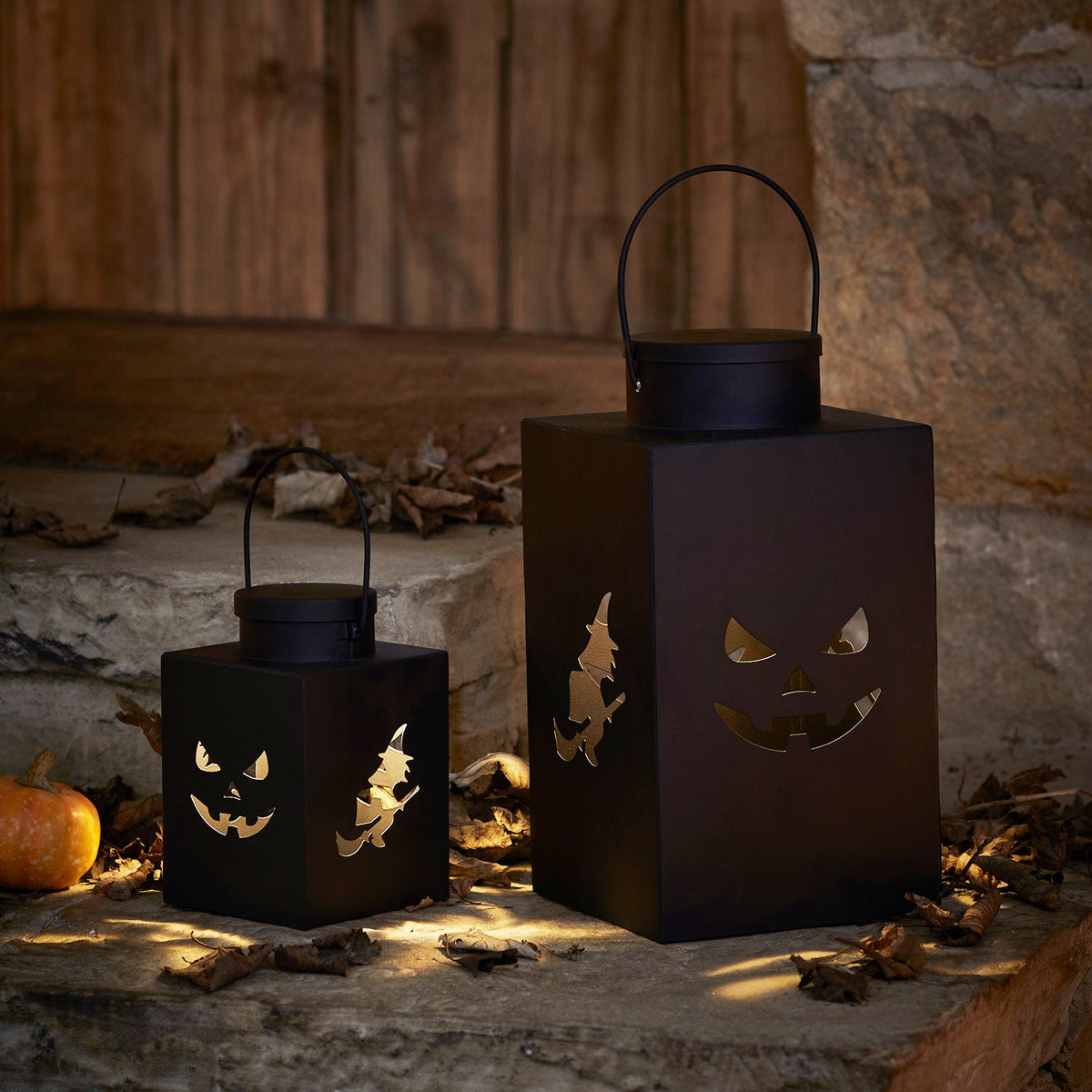 Zwei schwarze Halloween-Laternen aus Metall mit Kürbisgesicht und Hexe, beleuchtet auf Steinboden
