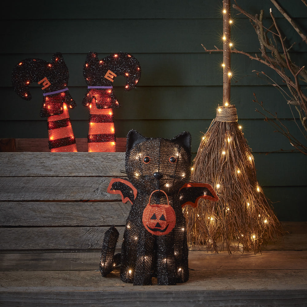 Halloween-Deko Fledermaus-Katze mit warmweißen LEDs neben Hexenbesen und gestreiften Hexenstiefeln
