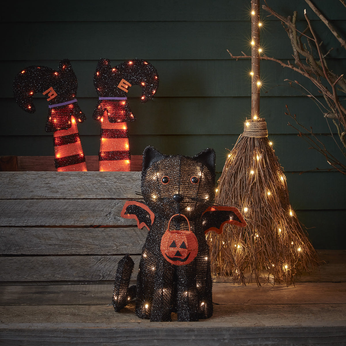 Halloween-Deko Fledermaus-Katze mit warmweißen LEDs neben Hexenbesen und gestreiften Hexenstiefeln