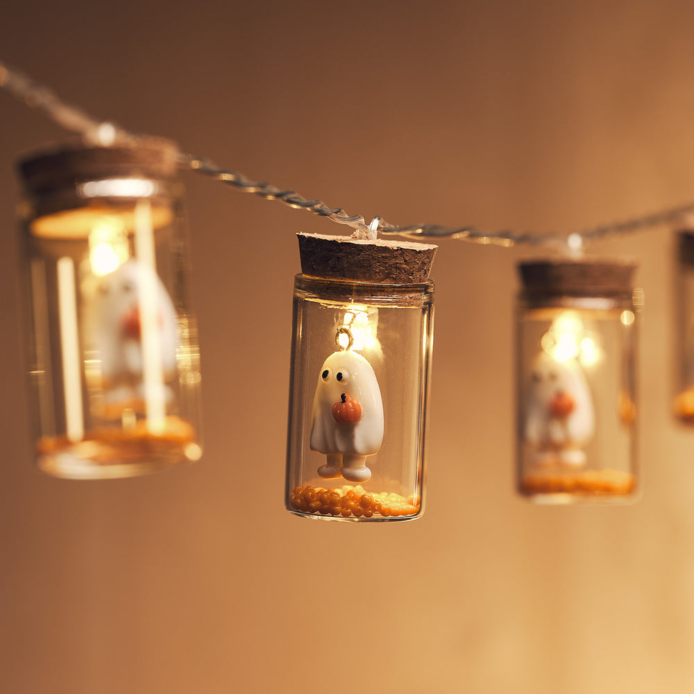 Nahaufnahme einer LED-Lichterkette mit kleinen Gläsern und Geisterfiguren mit Kürbissen