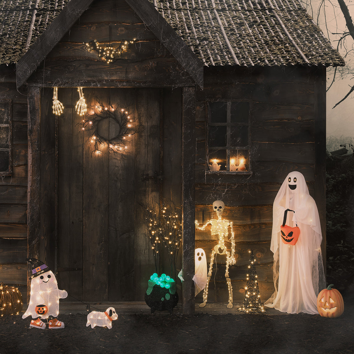 Halloween-Dekoration mit Geistern, Skelett und Kürbis vor dunklem Holzhaus
